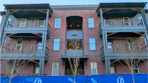 An image of a large new residential building with balconies and vintage style under blue skies near wide streets in Atlanta.