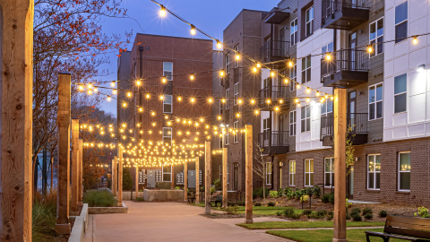 A photo of a large apartment complex with many lights near two wide streets near downtown Atlanta, under blue night skies.