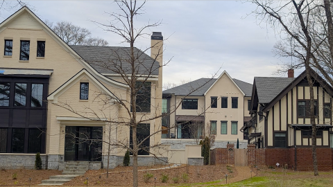 A photo of a large new development with many townhomes and large mansion dwellings around a new pool and large mansion in a Tudor Style. 