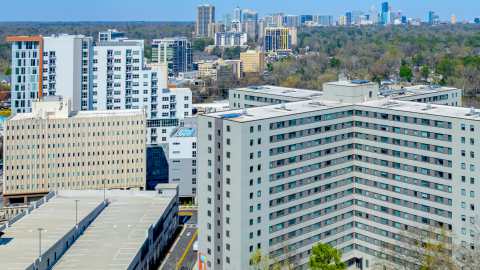 Photo of a renovated concrete housing tower in Atlanta under blue skies along a wide street with a dog park, pool, and modernized interiors near many trees.