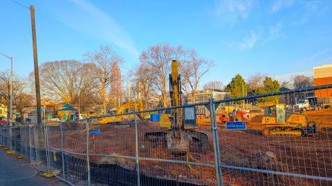 An image of a large red dirt construction site in Atlanta near many trees under blue skies with yellow heavy equipment across it.