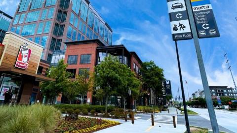An image of a large mixed-use district in Atlanta near wide road under blue skies with a new school taking one building. 