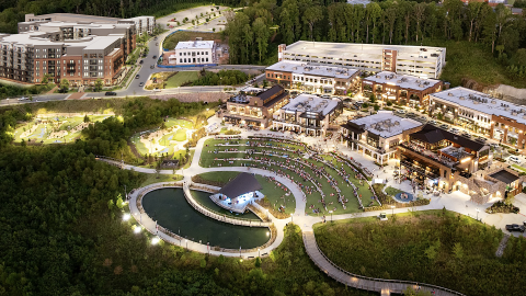 An overview of a large new apartment building next to many shops and restaurants around a large tiered park and pond. 