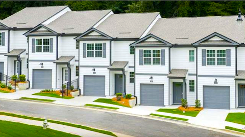A photo of a site where a row of white townhomes with gray garage doors and two stories on a new street now stands. 