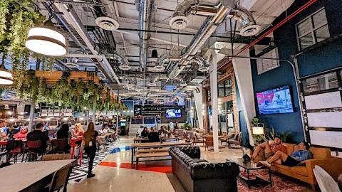 A huge brewery in Atlanta with tall ceilings and a huge bar beside the Beltline trail with many people inside.