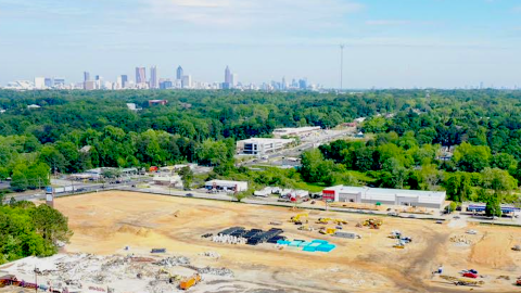 An aerial photo of a large construction site and green canopy and distant city.