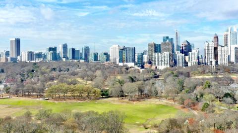 An aerial photo of Atlanta's skyline over a large green park under blue skies.