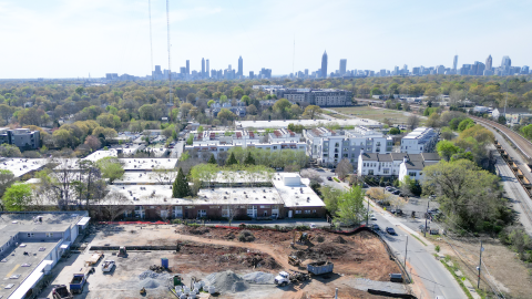 An aerial view over a corner on Atlanta's eastside with a large warehouse and construction site next to wide streets and a MARTA rail line