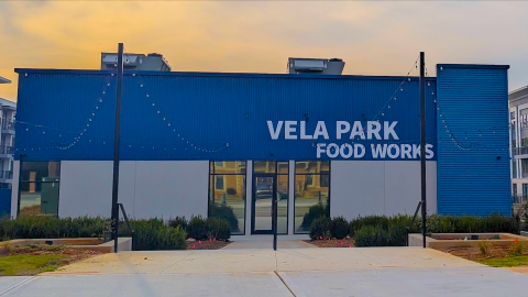 An image showing a large new apartment complex with blue and white exteriors under evening skies on Atlanta's eastside, with a food hall in the middle. 