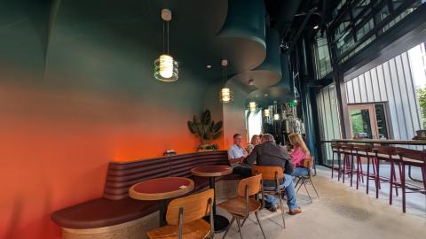 A photo of a large new modern brewery and restaurant space in blues and oranges with a huge patio and many trees in Atlanta near a wide walking and biking trail.