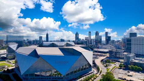 A photo of a large silver stadium in downtown Atlanta and a blue sky dotted with clouds over many buildings.