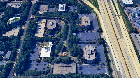 An overview of a huge office park area north of Atlanta next to a wide highway and many other buildings and houses and trees. 