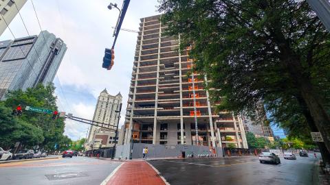 A photo of a large stripped and empty building under gray-blue skies in Atlanta near wide streets and trees.