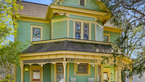 An image of a large old home in Decatur being offered as a short-term rental by a local college, with many trees around under blue skies.