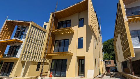 An image under blue skies of a large construction site with three modern homes and construction equipment and materials. 
