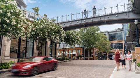 An image of a large shopping center with quaint streets and shops and trees under blue skies. 