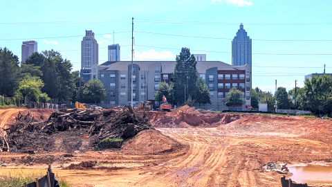 A photo of a large construction site in red earth with heavy equipment under a blue sky near a dog park in Atlanta.