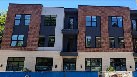 An image of a three-story brick building under blue skies in Atlanta with many windows on a street with many trees.