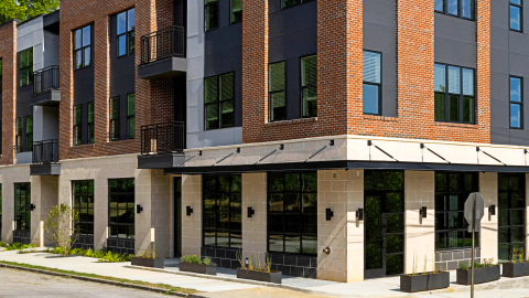 A photo of a new brick building with apartments on top of retail space in Atlanta near wide roads, under blue skies.