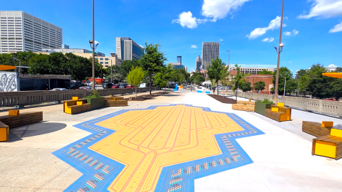 A photo of a large new seating area and public art areas near South Downtown Atlanta with a skyline in the distance and blue skies above.
