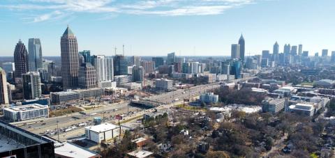 An image of a skyline under blue skies near a huge highway with many trees and smaller buildings at bottom. 